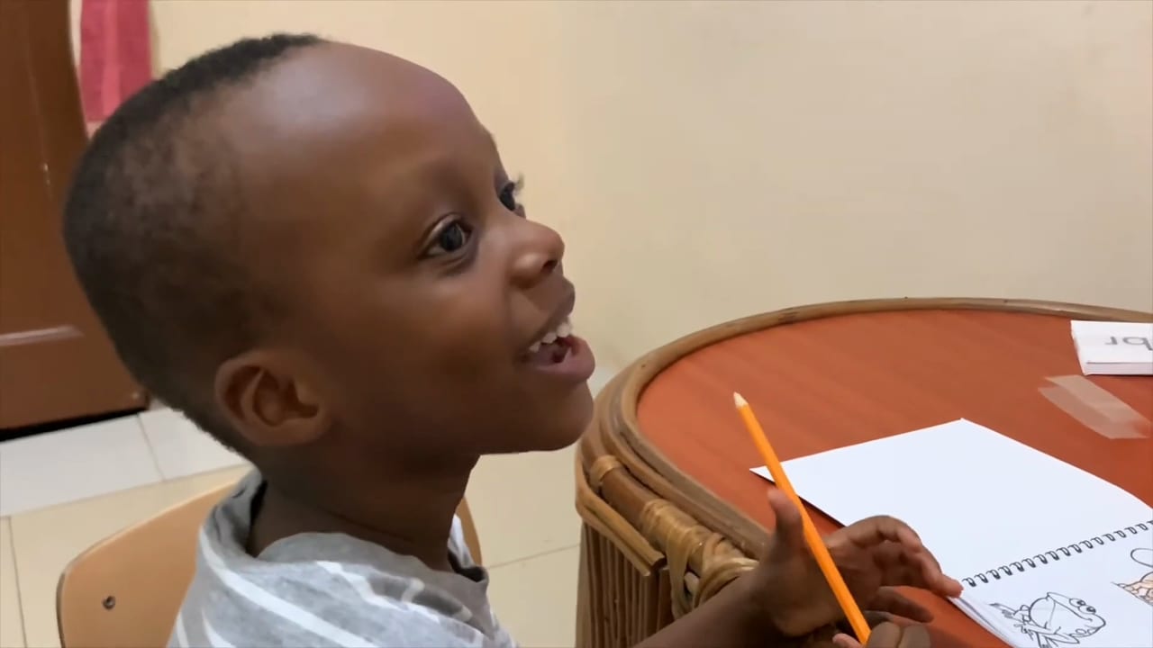 Anson smiling up from his reading workbook, pencil in hand